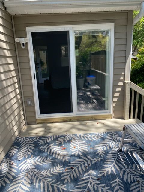 Sliding glass door to a deck with a blue leaf-pattern rug and beige siding.