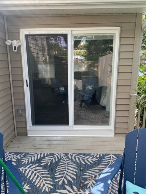 Sliding glass door with white frame and beige siding, opening to a deck with a blue leaf-pattern rug.