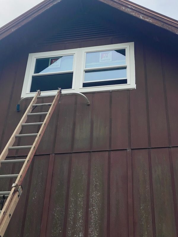 Ladder leaning against a brown house beneath a double window, with a white curved pipe below the sill