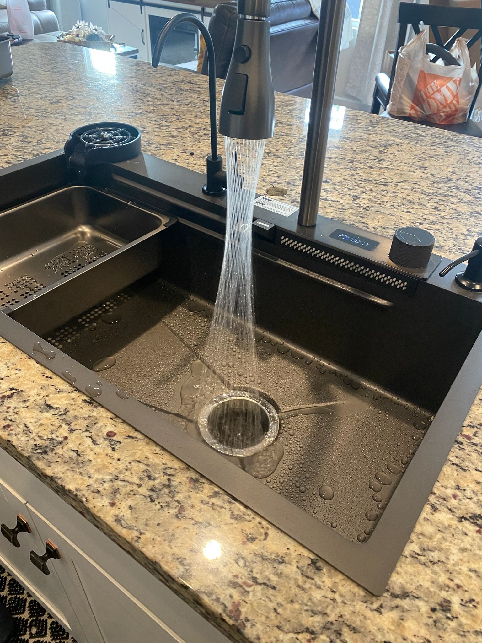 Kitchen sink with running water flowing into a black basin and granite countertop.