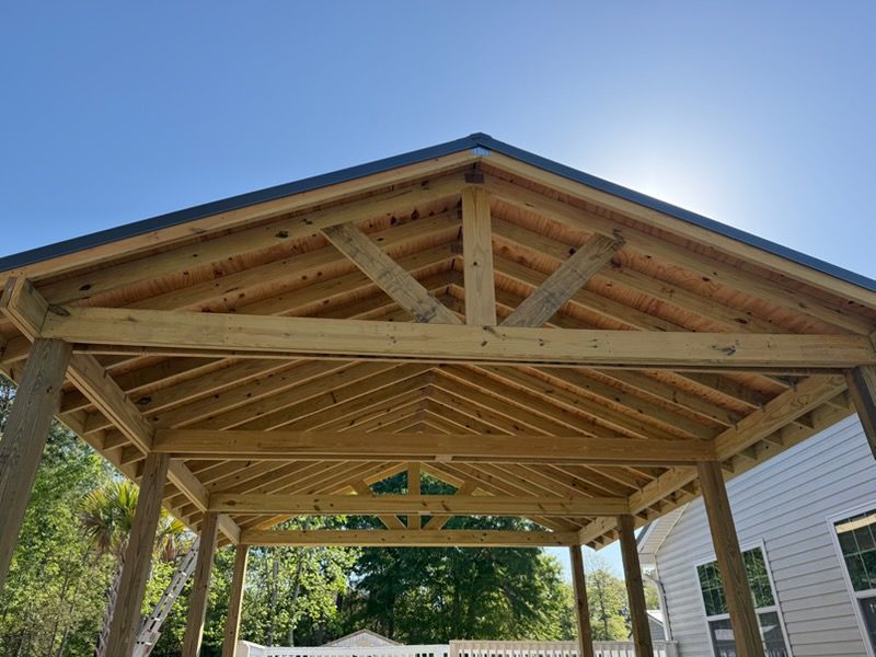 Wooden carport frame under construction beside a house on a sunny day