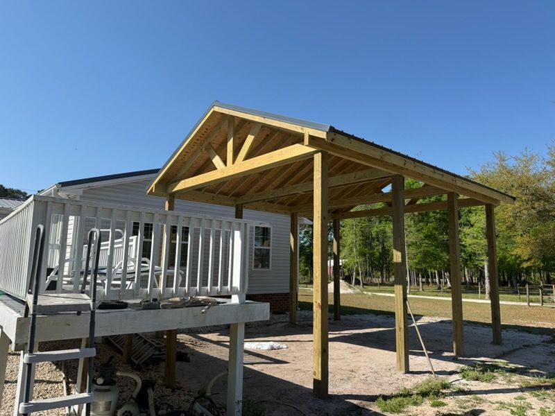 Wooden covered deck beside a house, with railings and support posts under a clear blue sky.