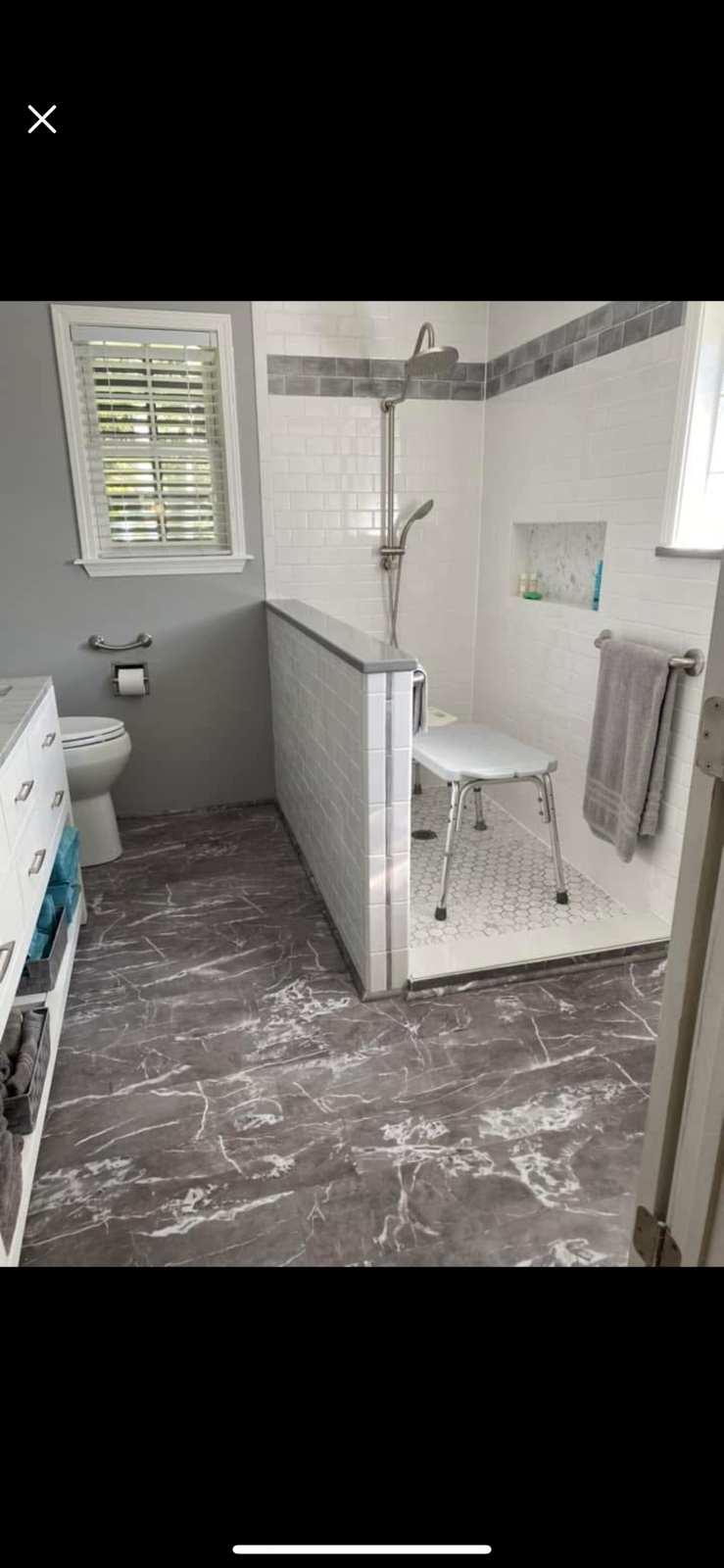 Small gray bathroom with walk-in shower, toilet, sink, and dark marble-style floor tiles.