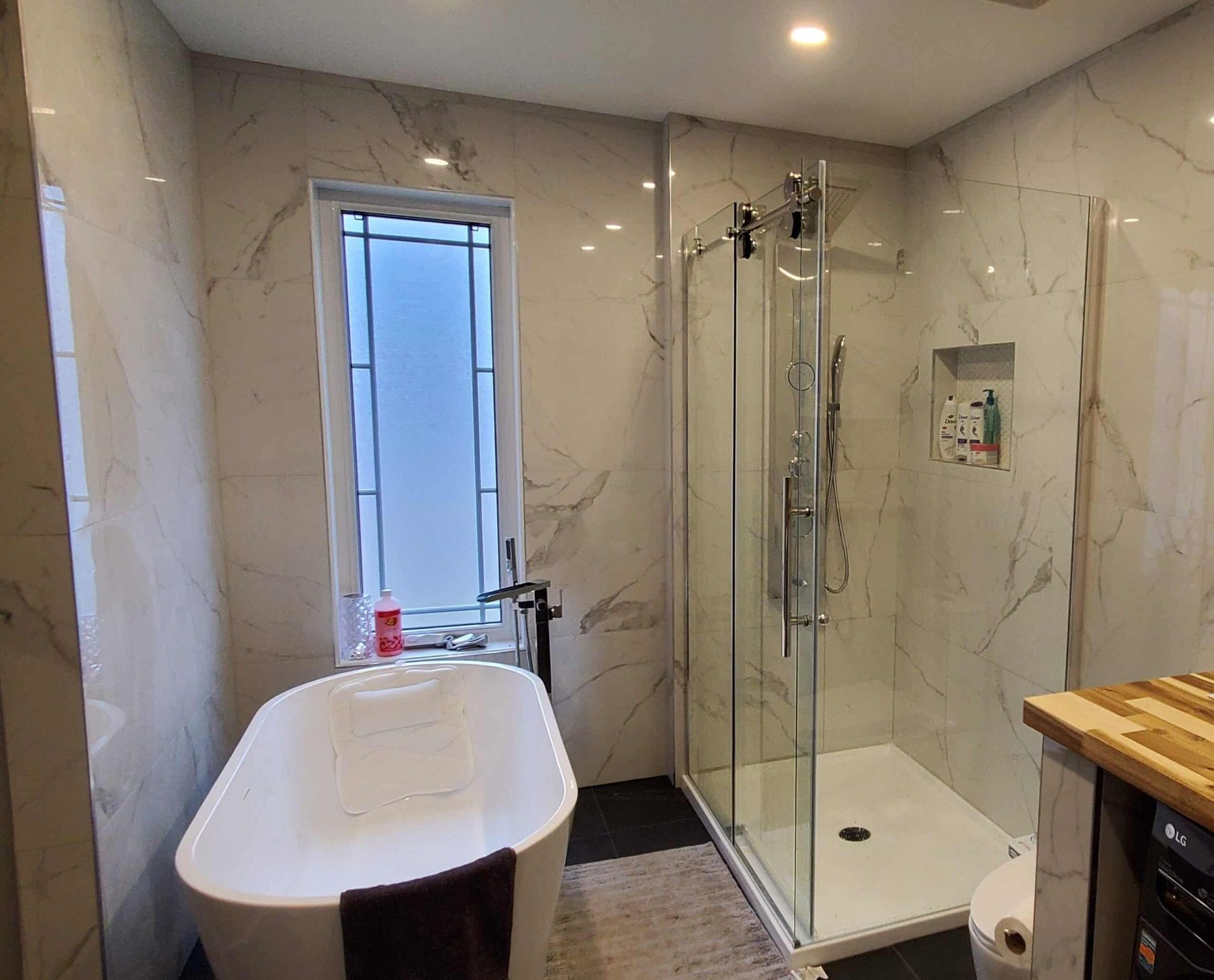 Salle de bains moderne avec carrelage en marbre blanc, baignoire îlot, douche en verre et petite fenêtre.