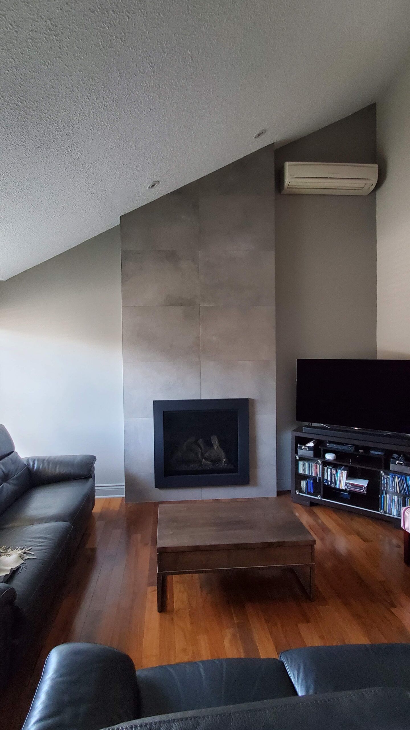 Salon avec cheminée, canapé et meuble TV. Les murs sont gris.