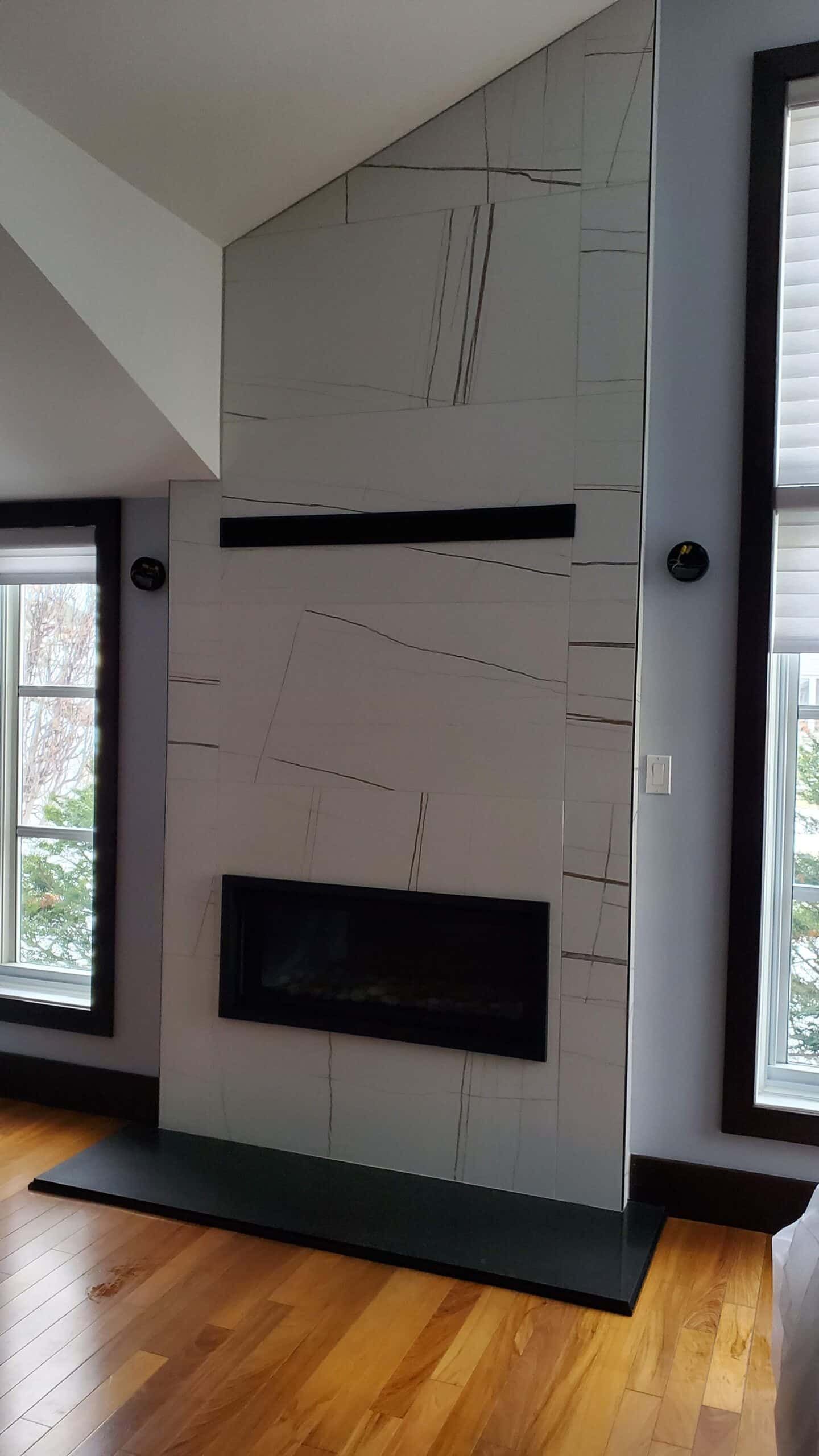 Cheminée en pierre gris clair, avec des moulures noires et un foyer noir, dans une pièce au parquet en bois dur.
