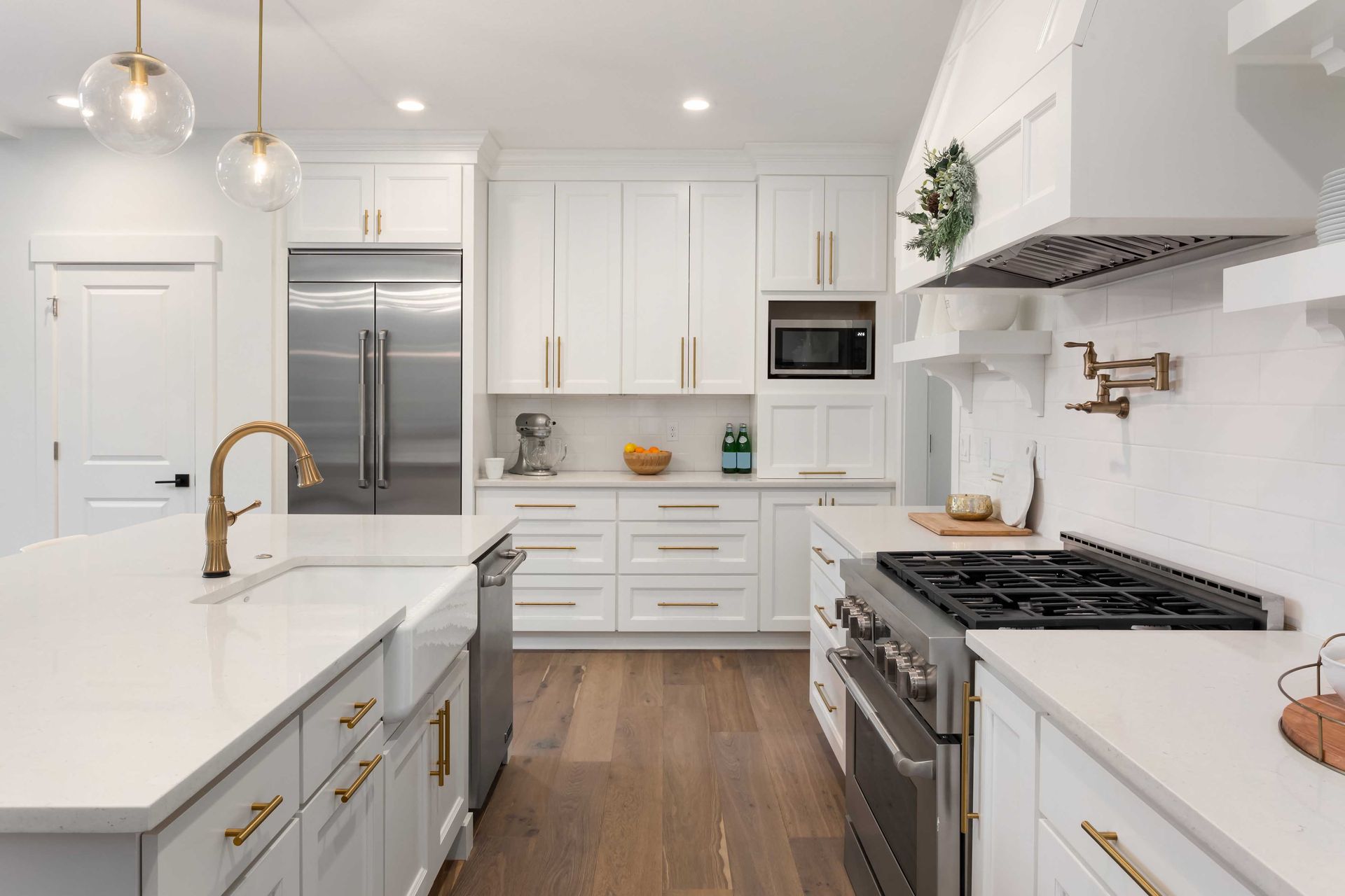 Cuisine lumineuse et blanche avec électroménagers en acier inoxydable, plancher en bois et grand îlot.