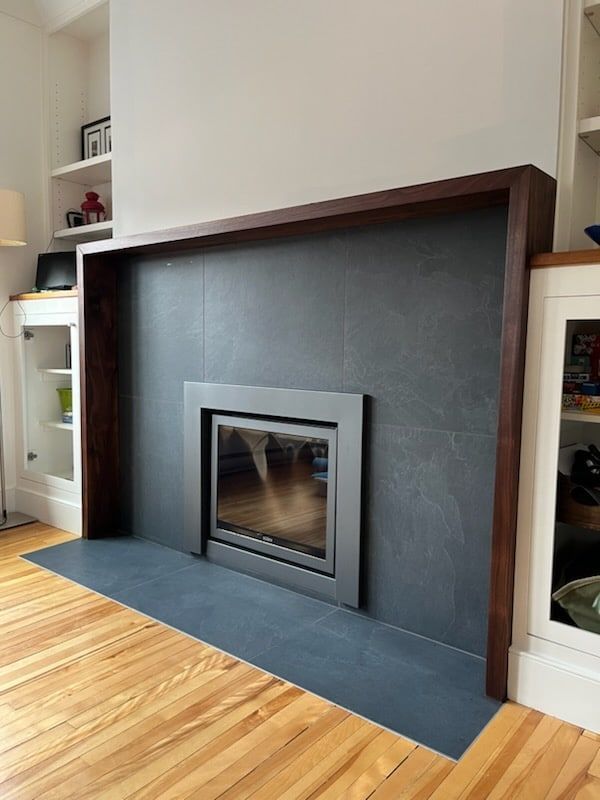 Cheminée avec ardoise gris foncé et garnitures en bois foncé, avec bibliothèques intégrées de chaque côté, parquet.