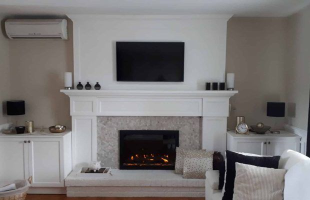 Cheminée avec télévision fixée au mur, encadrée par des meubles blancs. La décoration comprend des bougies, des haut-parleurs et des coussins.
