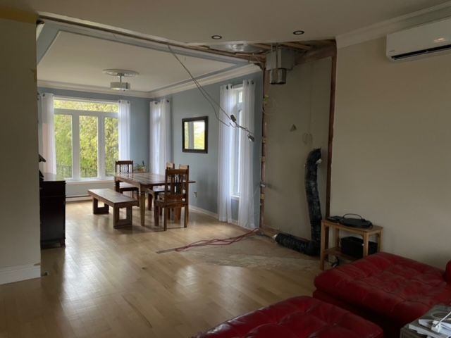 Vue intérieure d'une pièce en construction, avec un mur apparent et un coin repas visible.