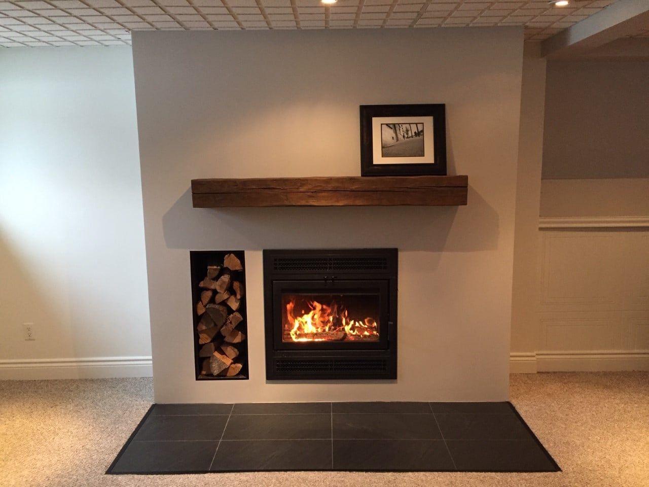 Cheminée avec feu allumé, rangement pour le bois et manteau en bois.