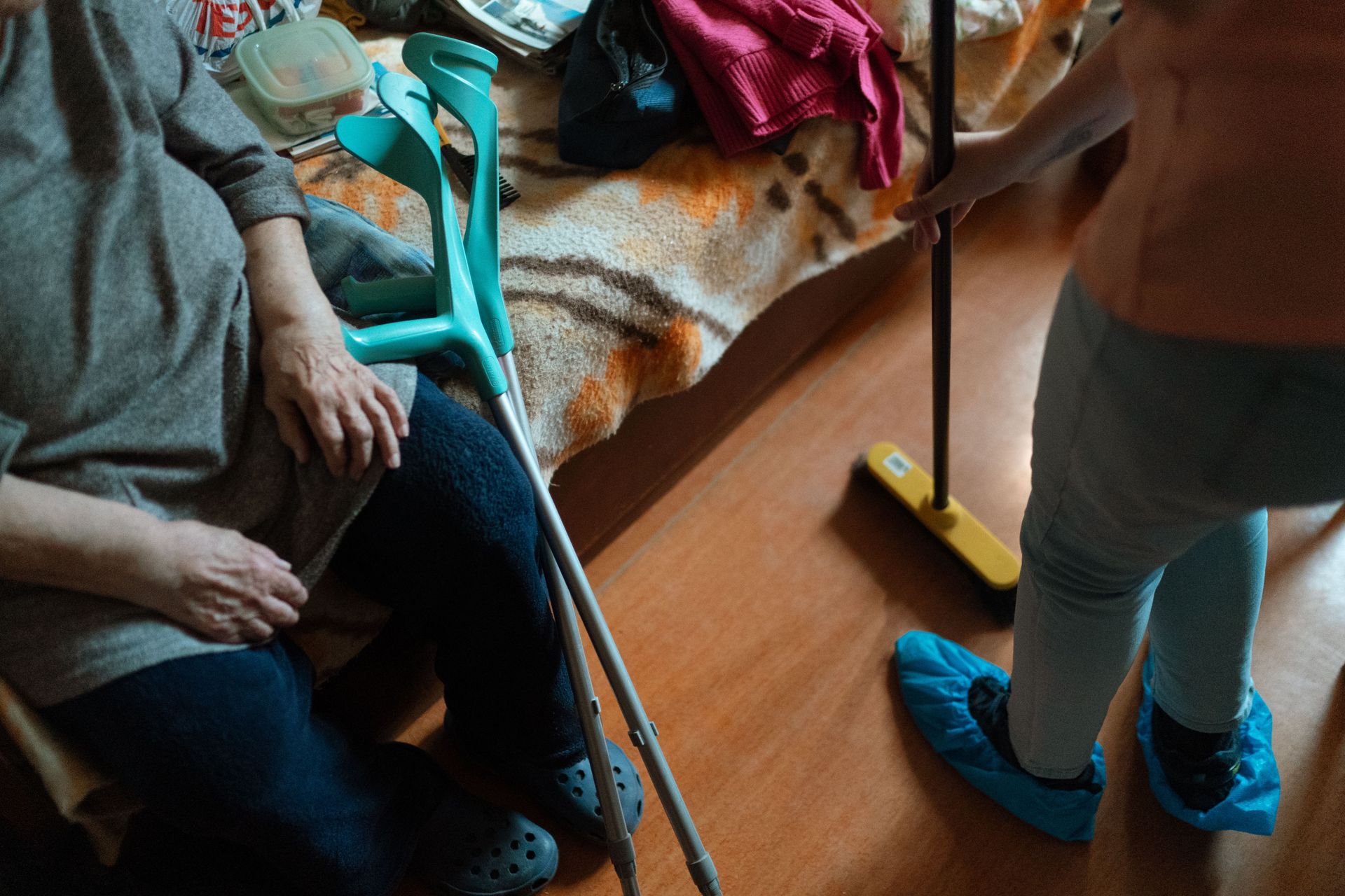 A healthcare worker in blue scrubs assists a person using a metal walker in a brightly lit room.