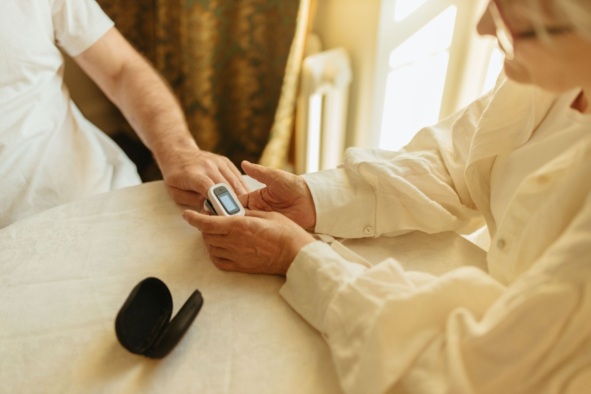 A healthcare professional in scrubs reviews paperwork with a patient at a wooden table in a home setting.