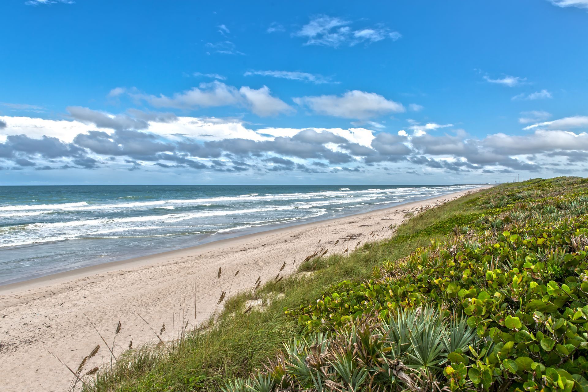 A sandy beach with waves crashing on the shore on a sunny day.