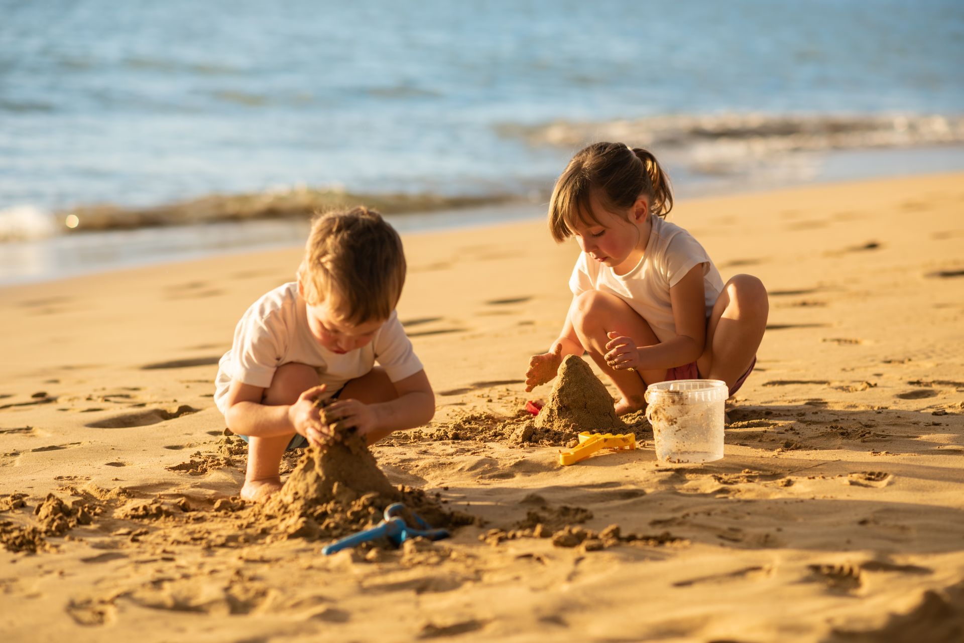 A boy and a girl are playing in the sand on the beach.
