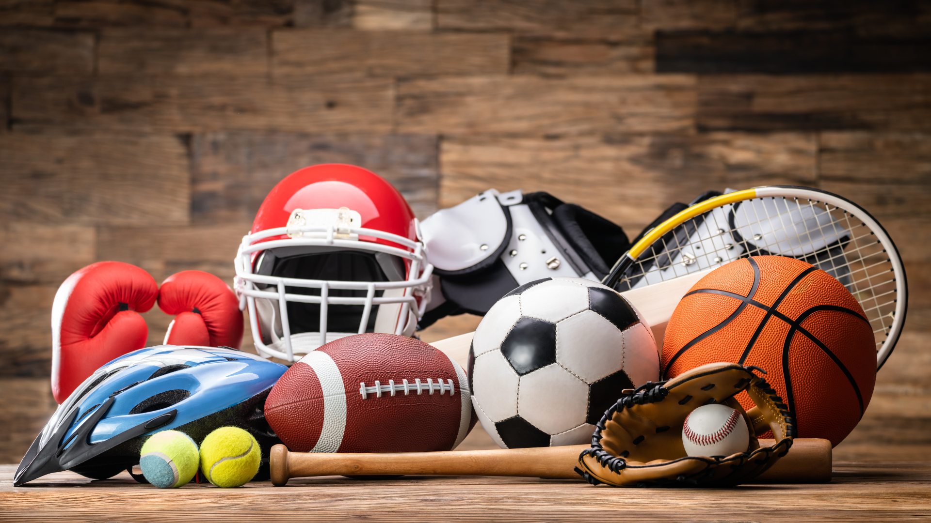 Sports equipment: football helmet, boxing gloves, basketball, soccer ball, baseball, tennis racket, bat, and more on wood.