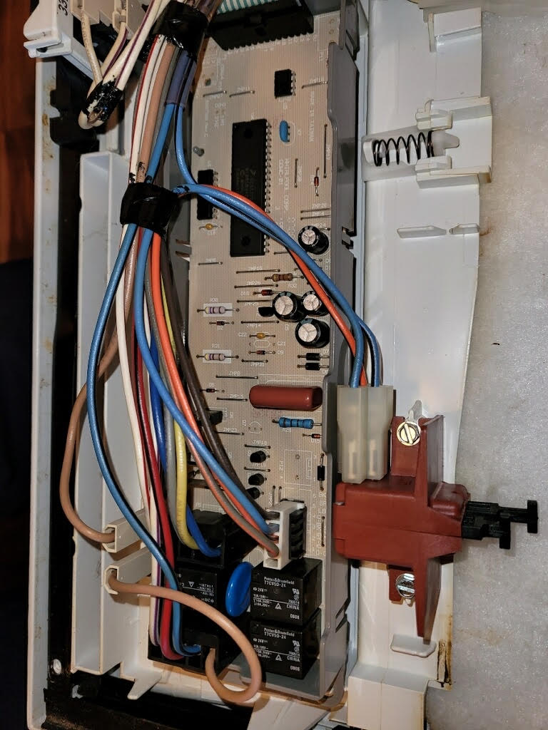 An interior view of a white plastic appliance housing showing a circuit board with connected multi-colored wiring bundles.