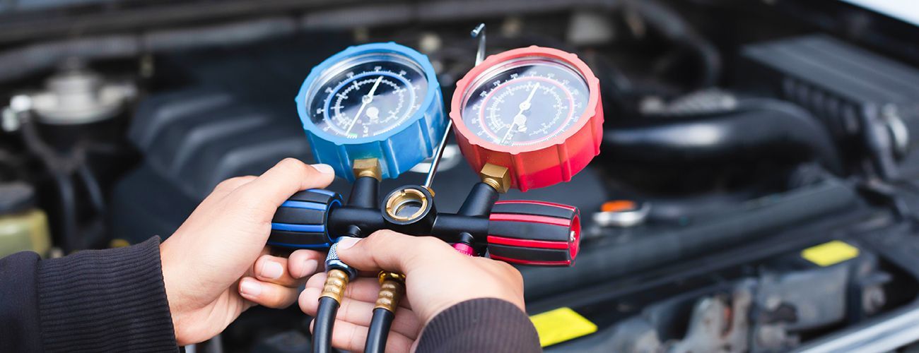Hands holding air conditioning gauges over a car engine.