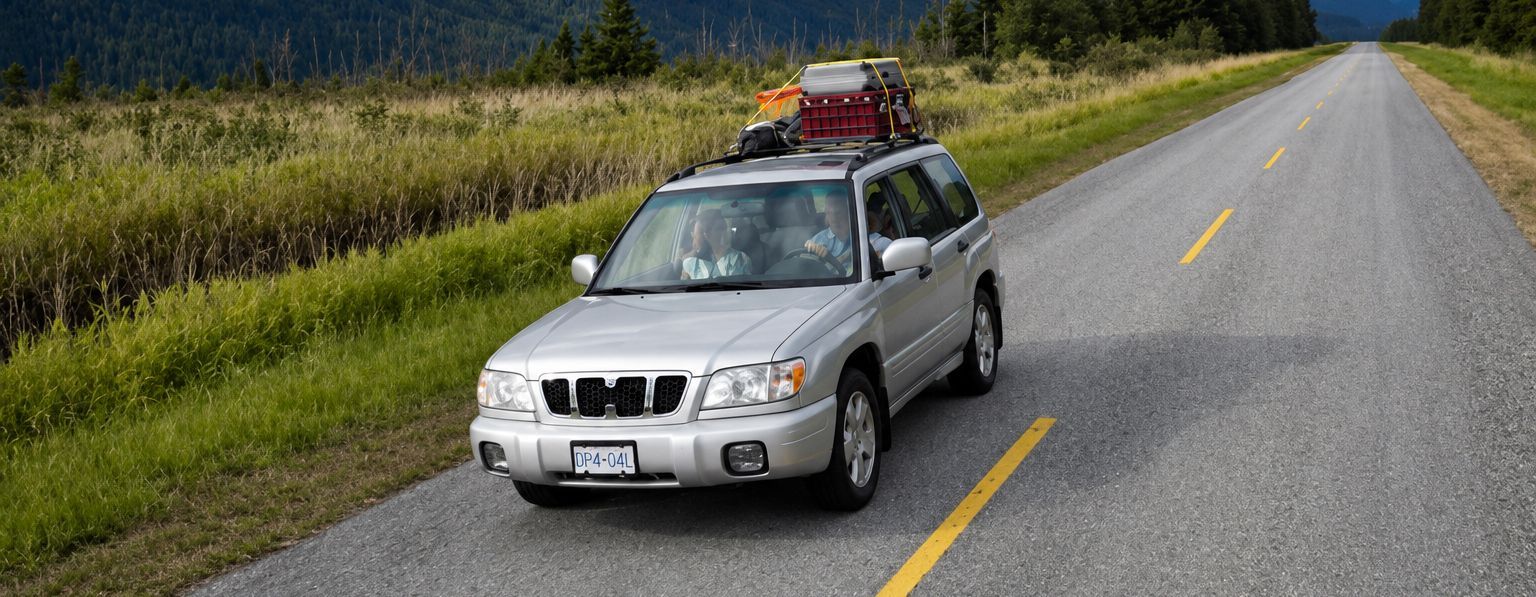 Silver SUV with roof cargo driving on a rural road beside green fields