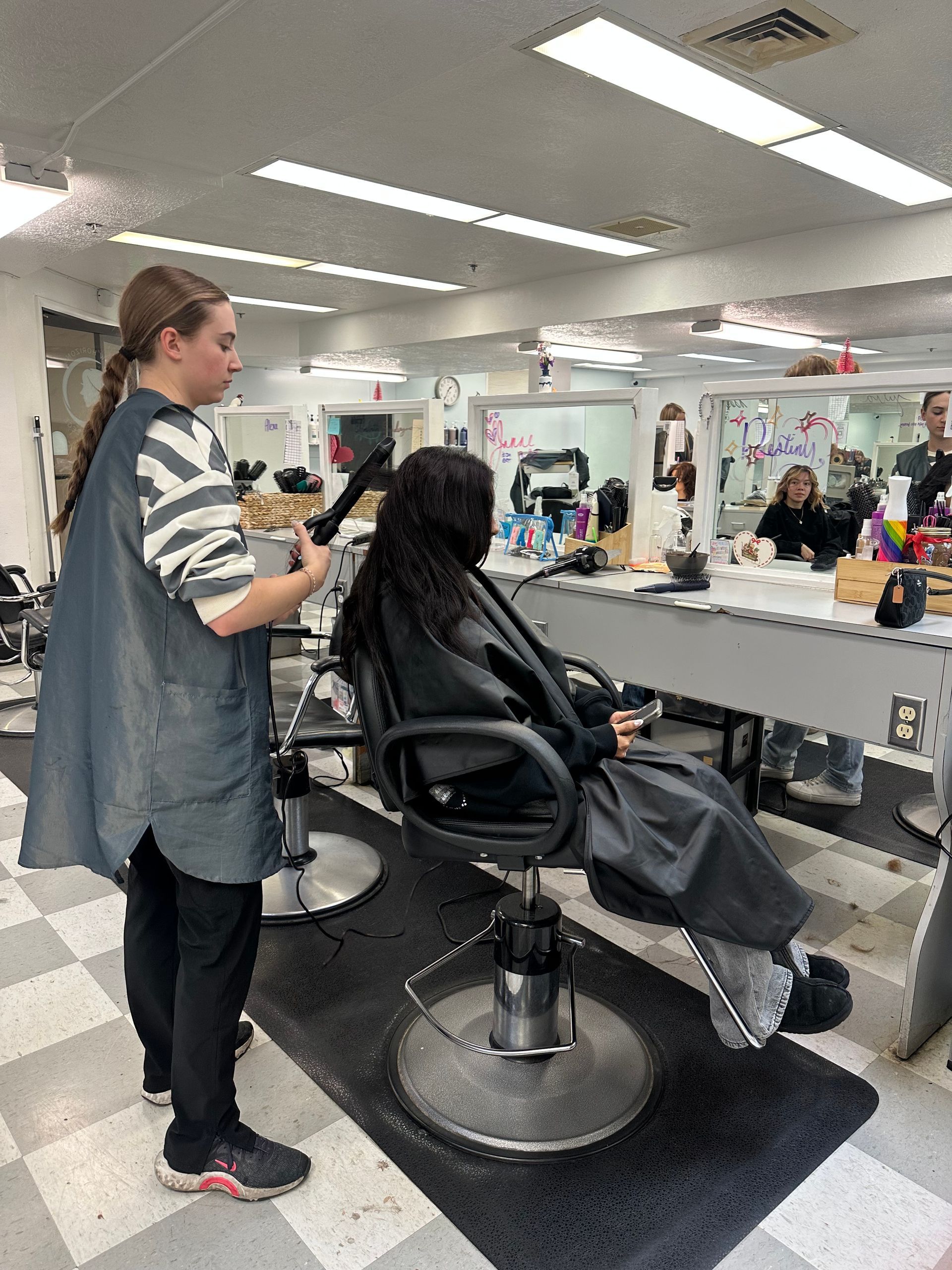 A stylist uses a curling iron on a client's hair in a brightly lit hair salon.