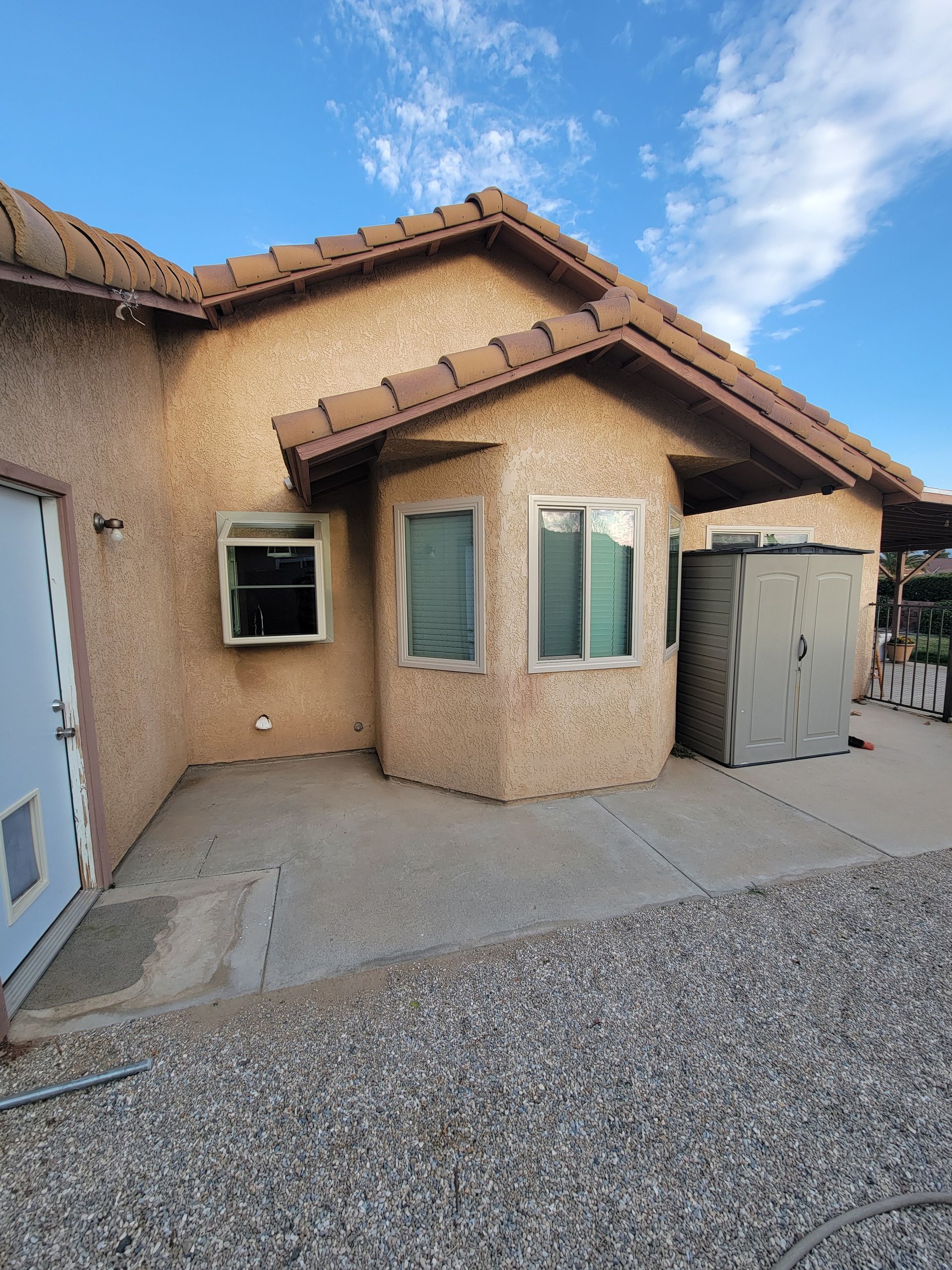 Stucco house exterior with bay window, gravel driveway, and blue sky.