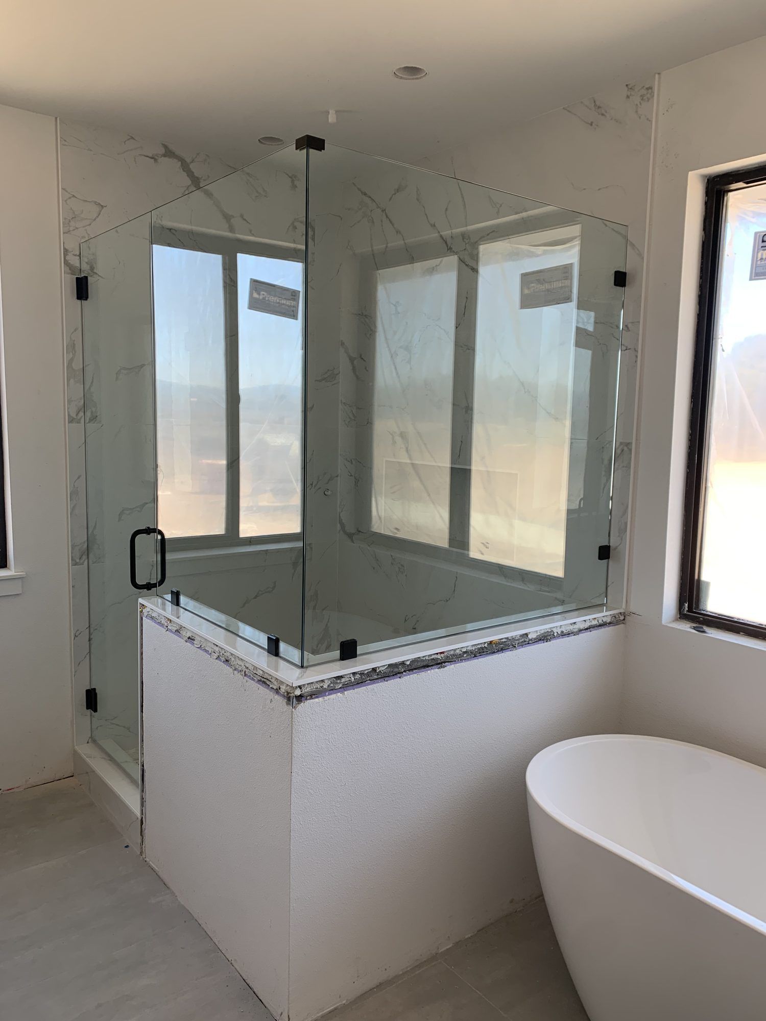 Angular frameless shower enclosure on a knee wall beside a freestanding tub