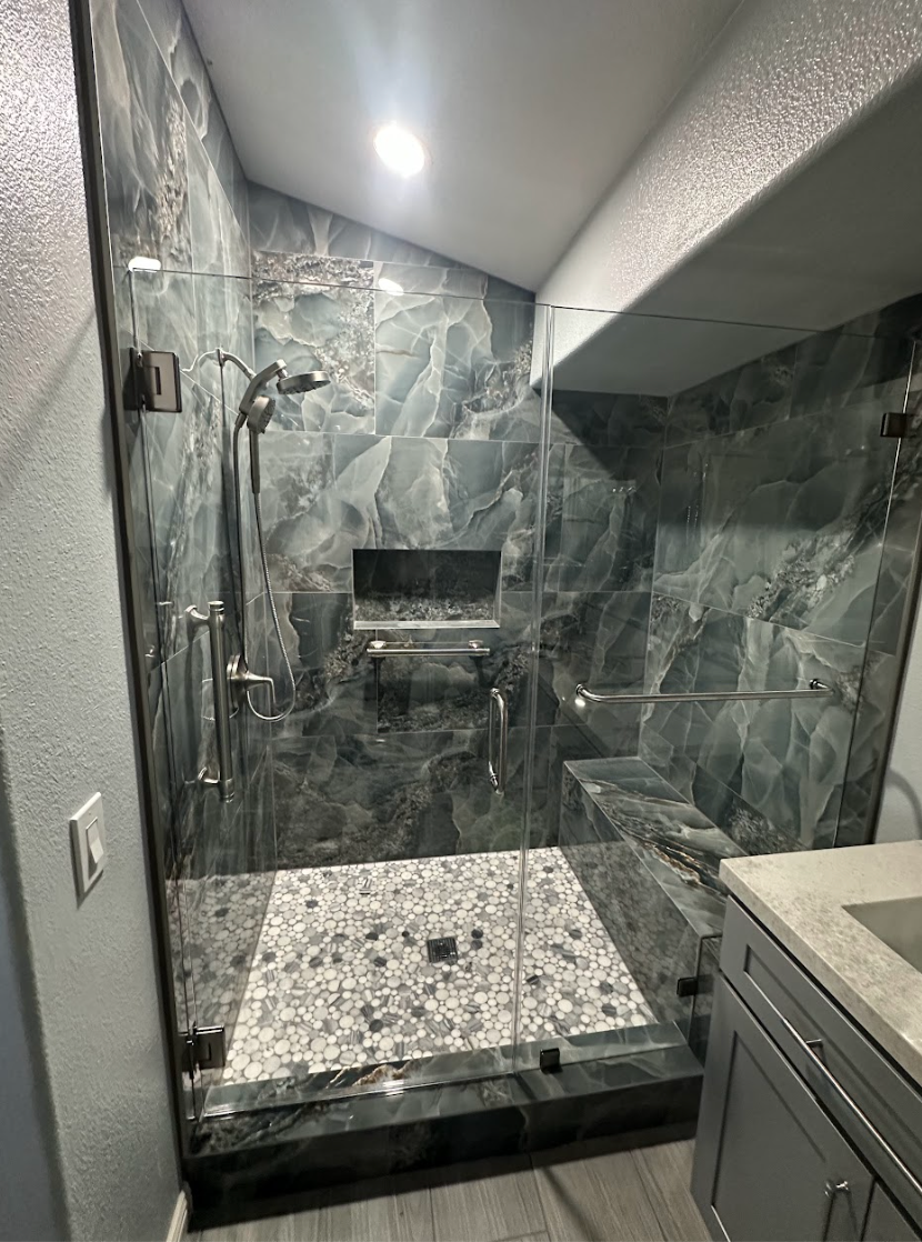 Frameless hinged glass shower door with dark marble tile and brushed nickel hardware by High Desert Window and Glass