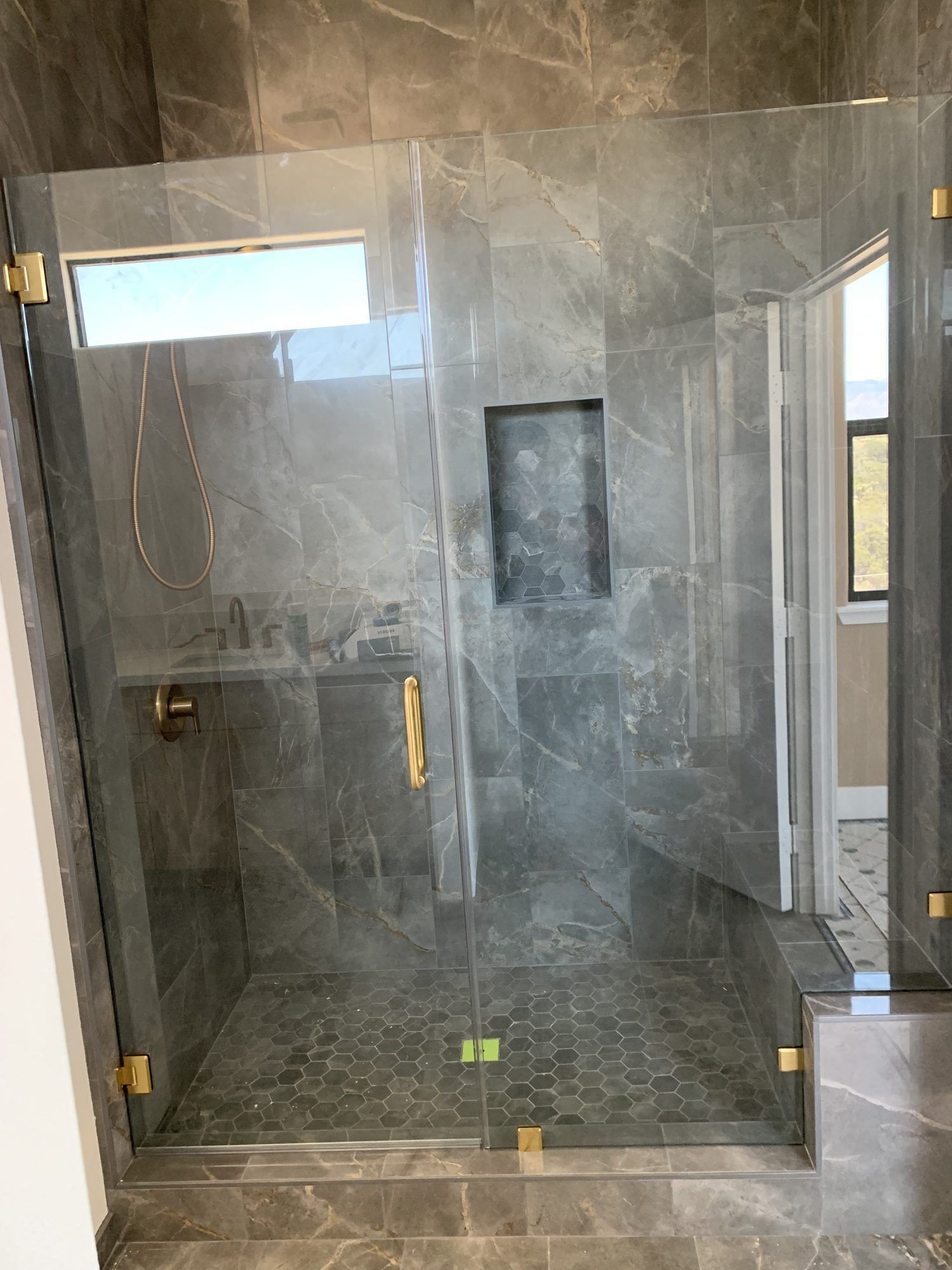 Frameless glass shower enclosure with gold hinges and gray tile by High Desert Window and Glass