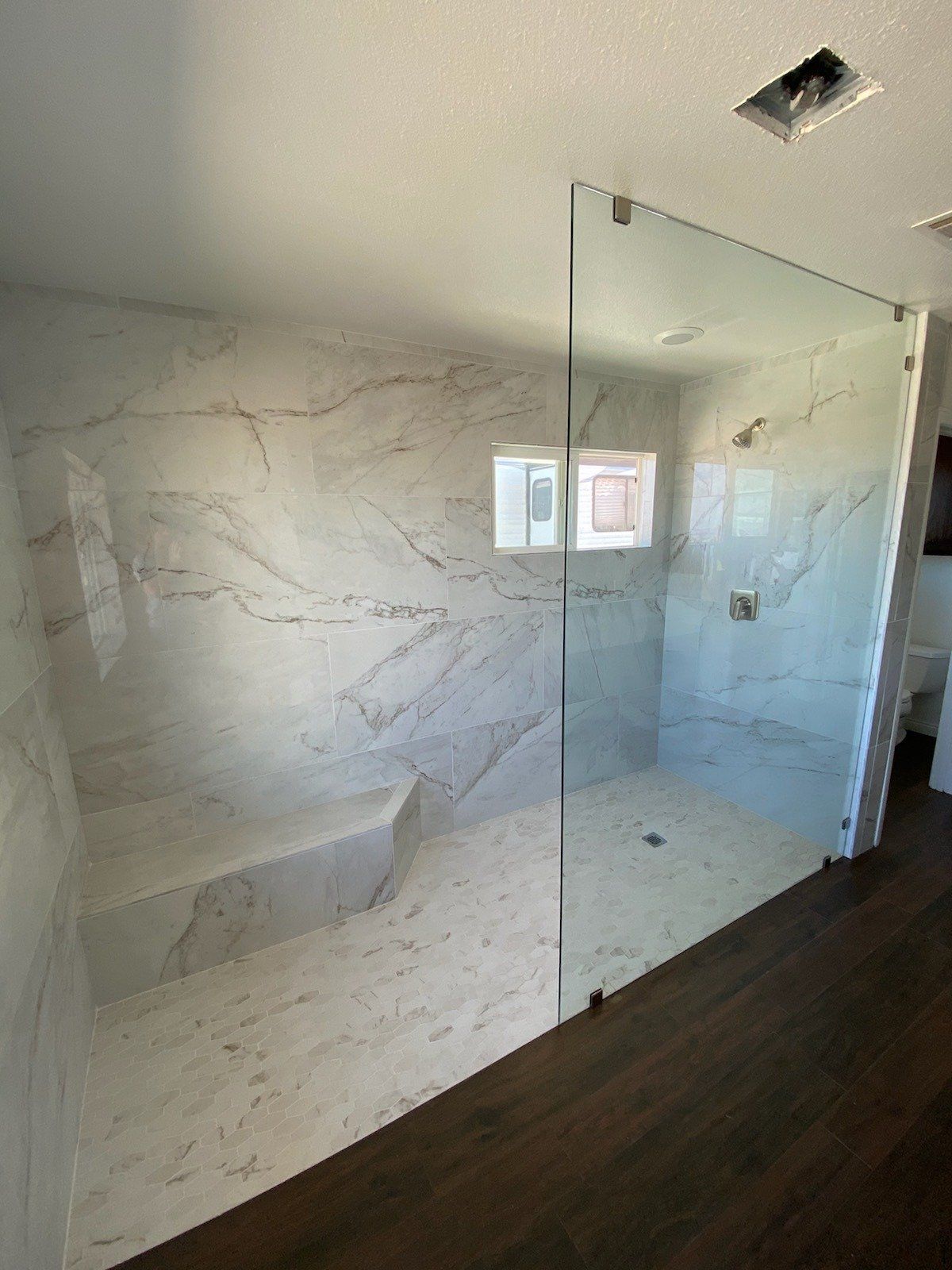 Frameless walk-in shower glass panel with marble tile