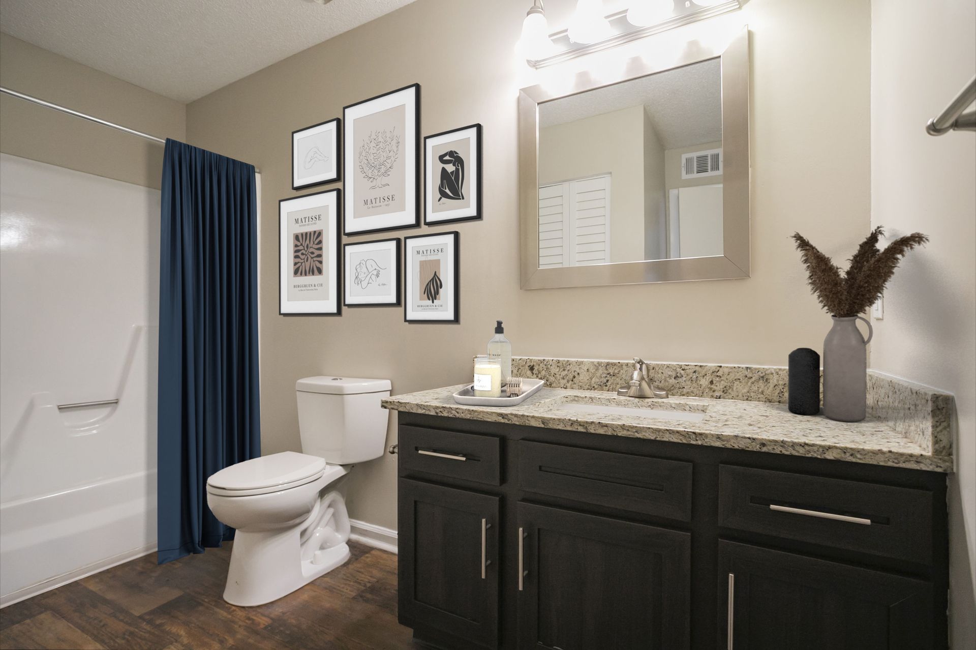 A modern bathroom with dark cabinets, granite countertops, a toilet, a bathtub with a navy curtain, and framed wall art.
