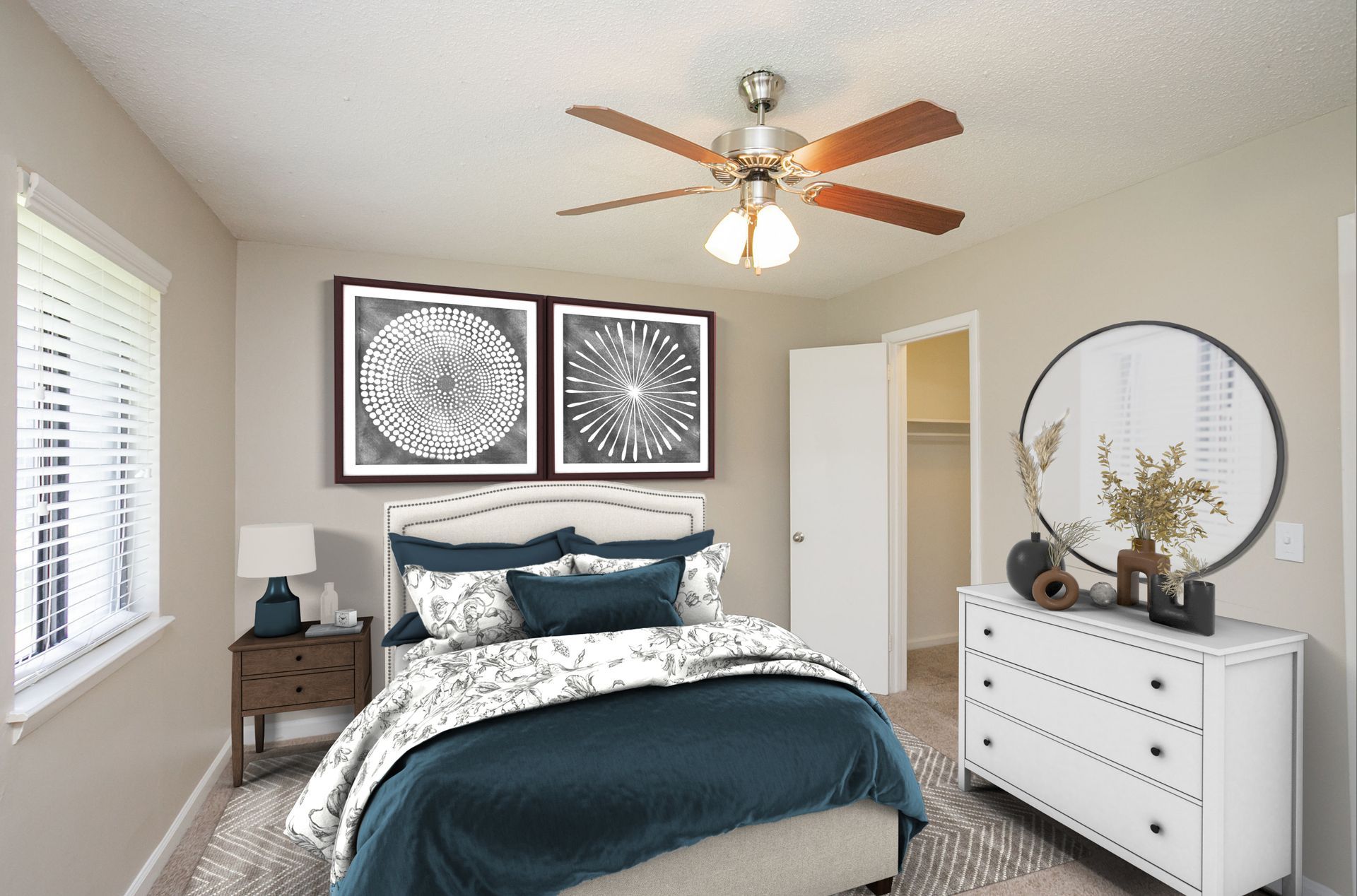 A cozy bedroom featuring a bed with navy and white bedding, a white dresser with a circular mirror, and a ceiling fan.