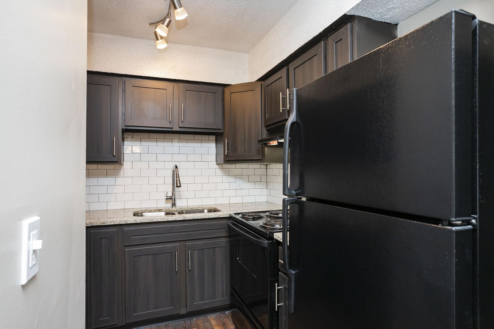 A galley kitchen with dark wood cabinets, a black refrigerator and stove, and a white subway tile backsplash.
