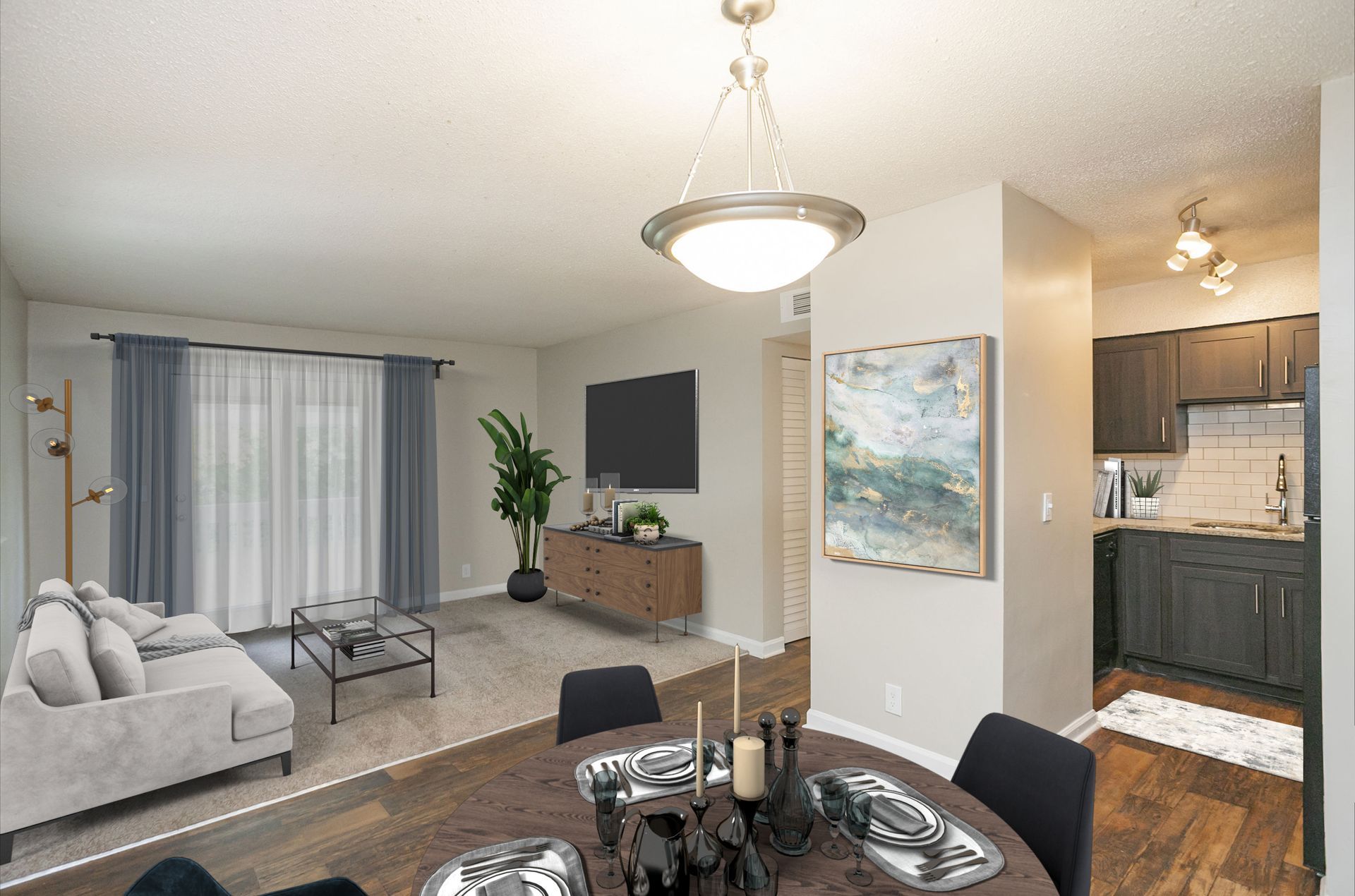 A bright, open-concept apartment with a dining area in the foreground, living room with gray sofa, and kitchen beyond.