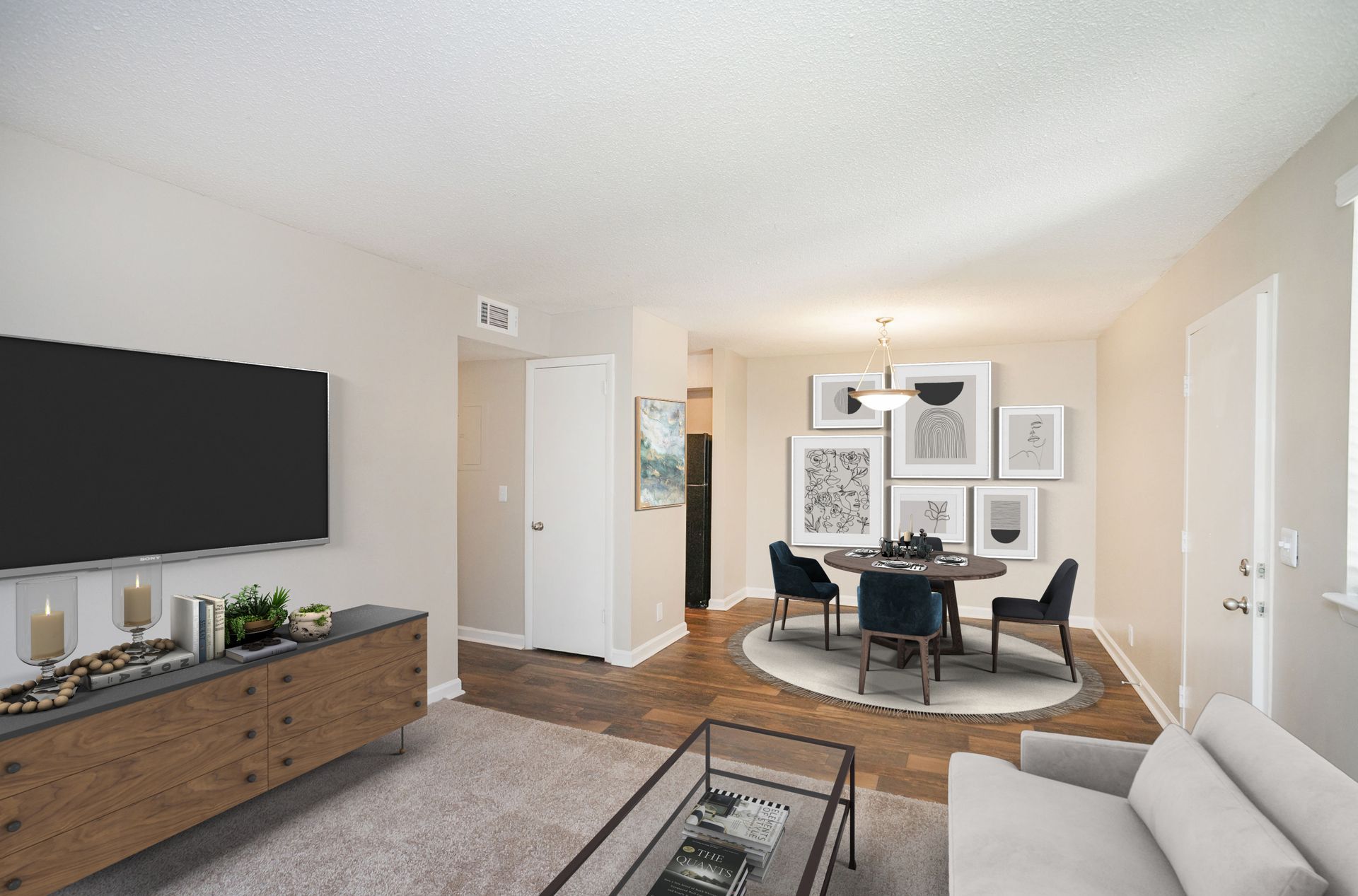 A bright apartment living room with a TV, a wooden media console, a grey couch, and a dining area with a table for four.