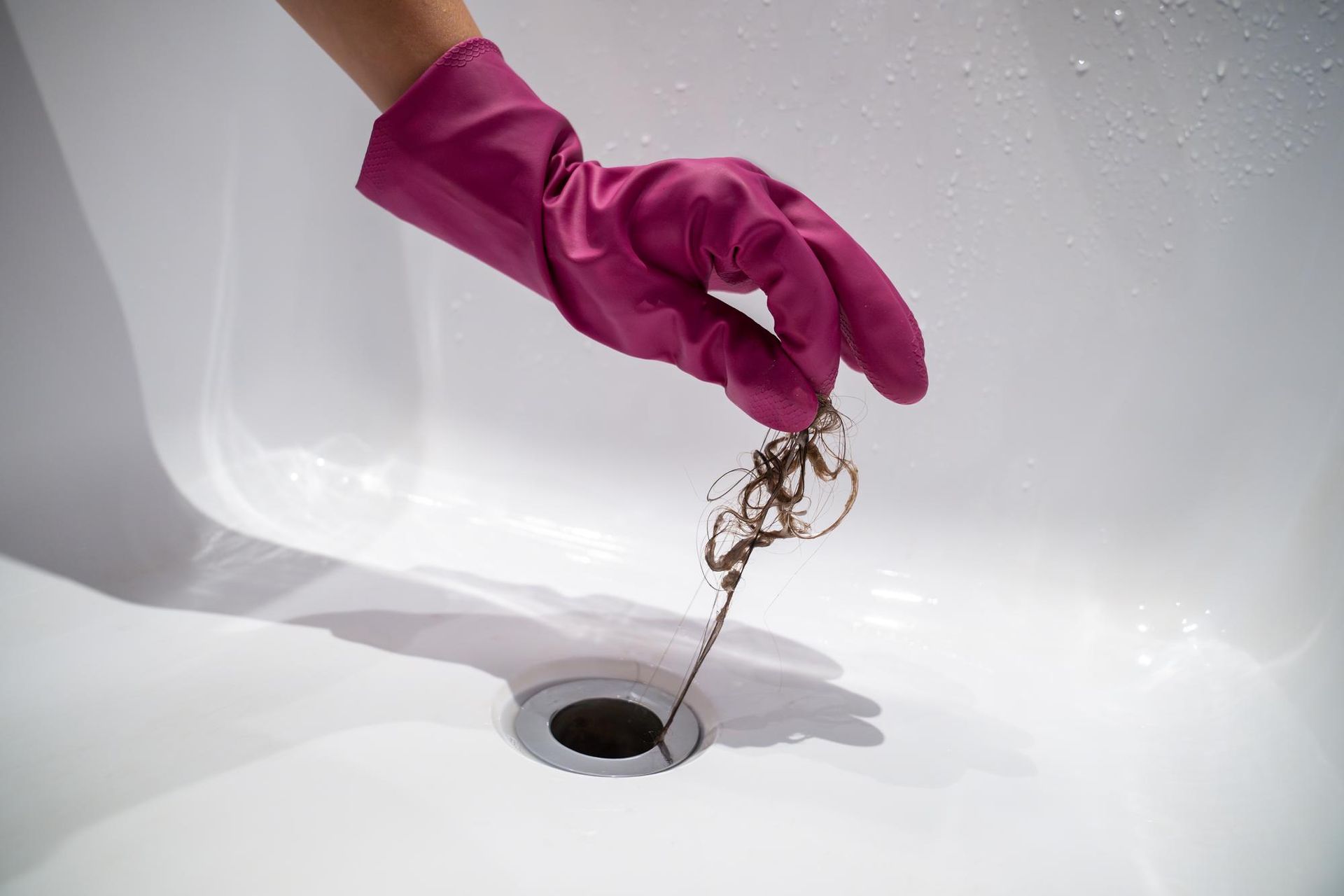 A person wearing pink gloves is cleaning a sink drain.
