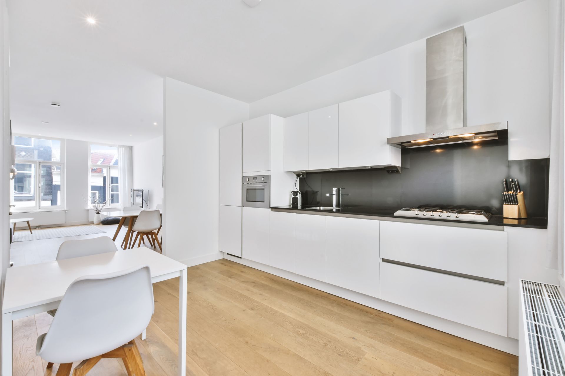A kitchen with white cabinets , wooden floors , a table and chairs.