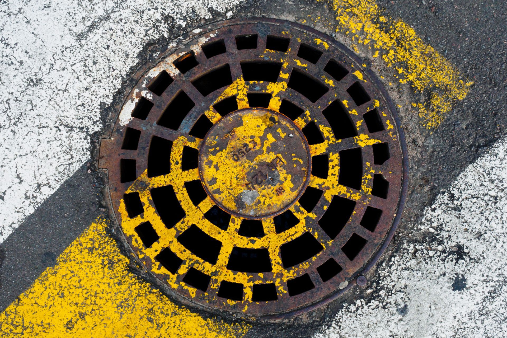 A manhole cover is painted yellow and black on the side of the road.