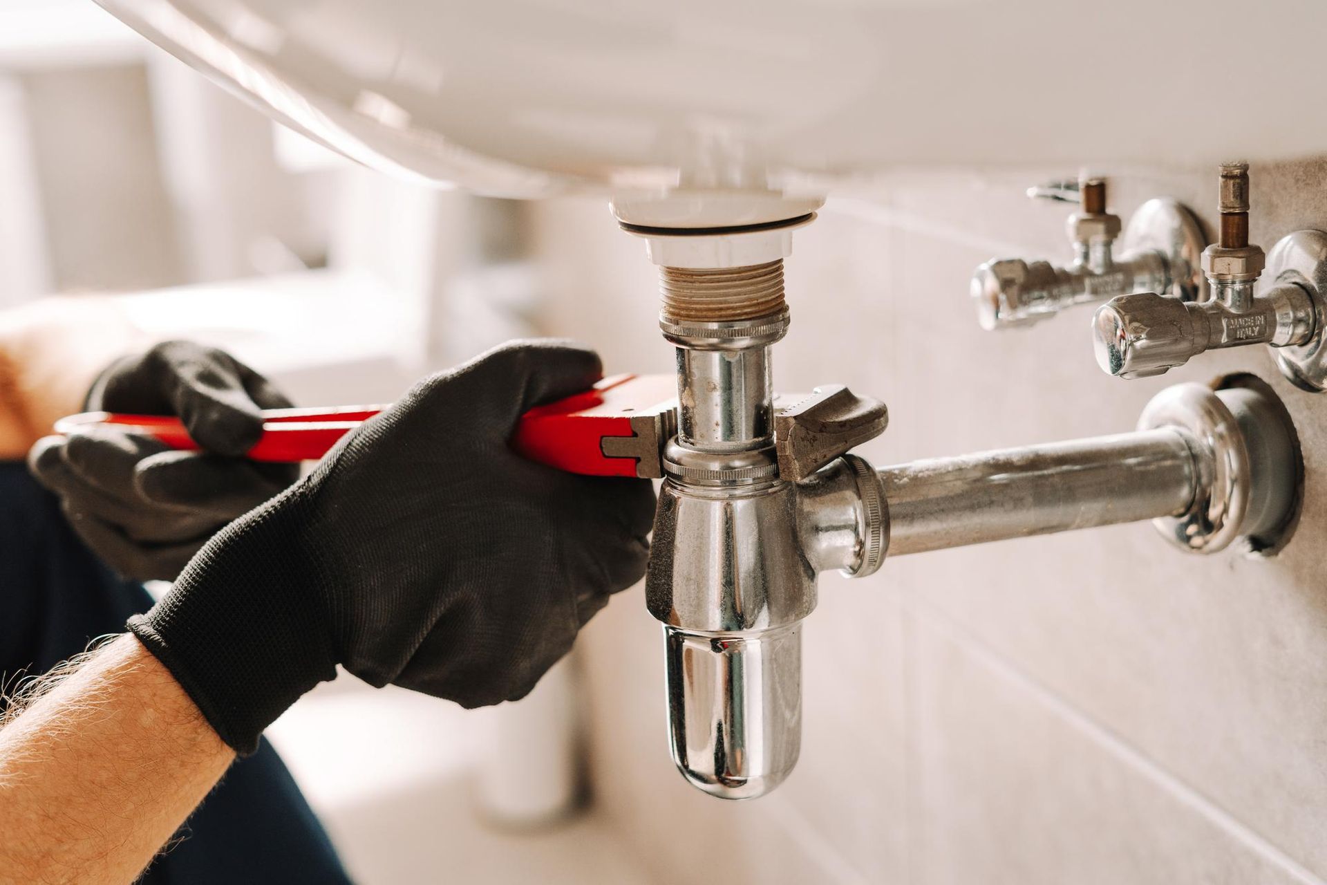 A plumber is fixing a sink pipe with a wrench.