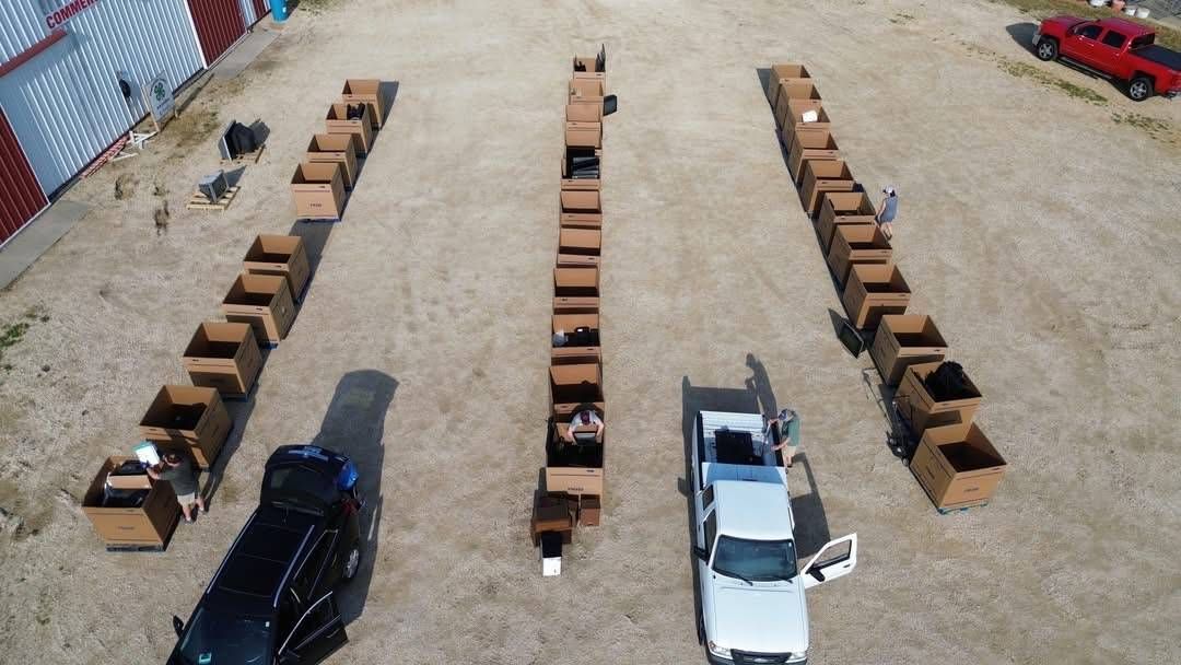 Aerial view of vehicles unloading electronics into rows of collection boxes at a community recycling event