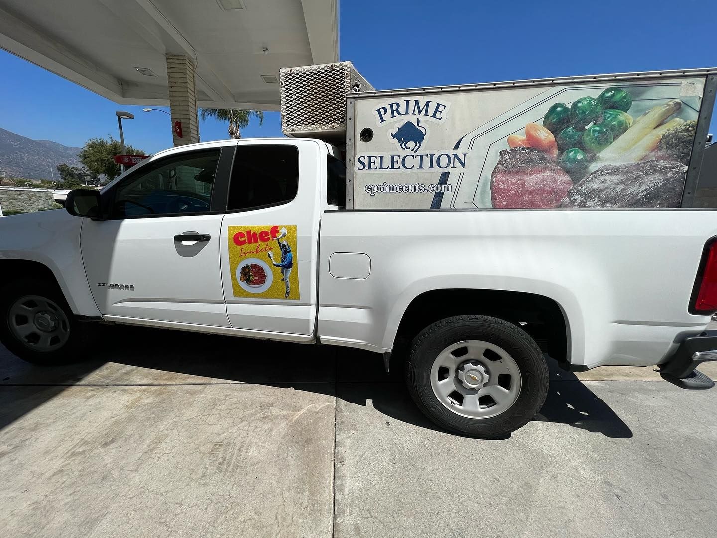 White pickup truck with fruit stand graphics parked at a gas station pump under a canopy. White pickup truck with fruit stand graphics parked at a gas station pump under a canopy.