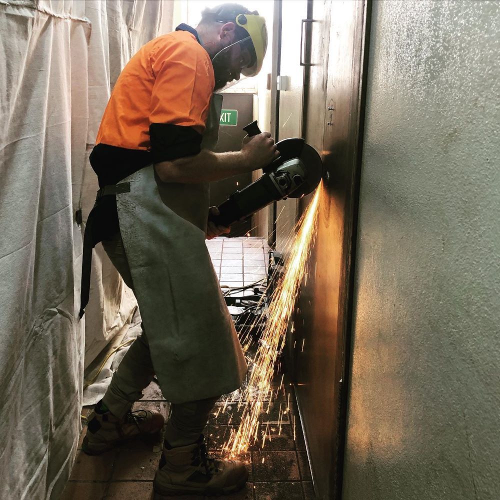 A Man Is Using a Grinder on A Wall — Toowoomba Locksmiths in Lockyer Valley, QLD