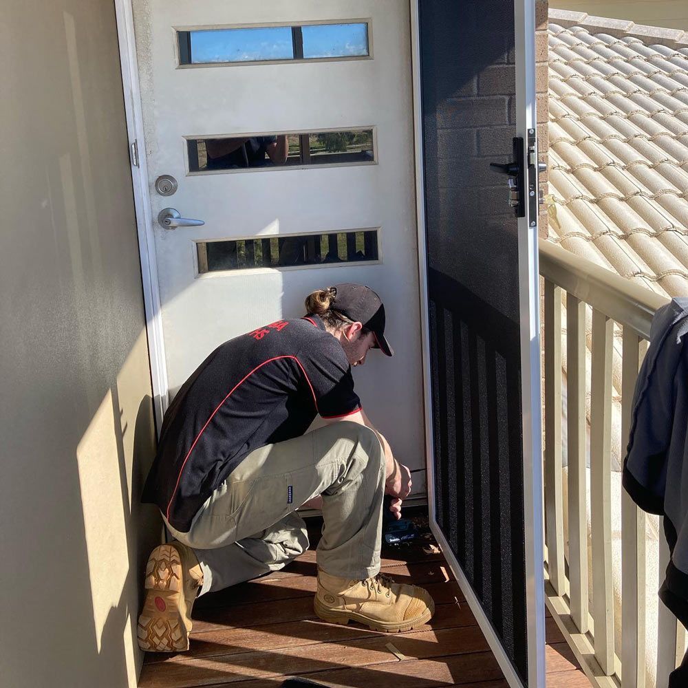A Man Is Kneeling Down in Front of A Door — Toowoomba Locksmiths in Toowoomba City, QLD
