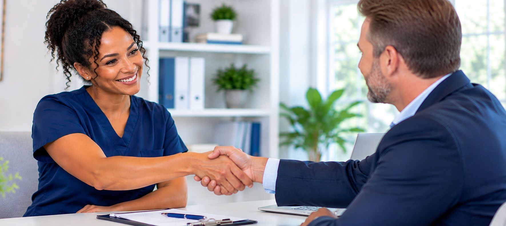 Two people shaking hands across a desk in a bright office