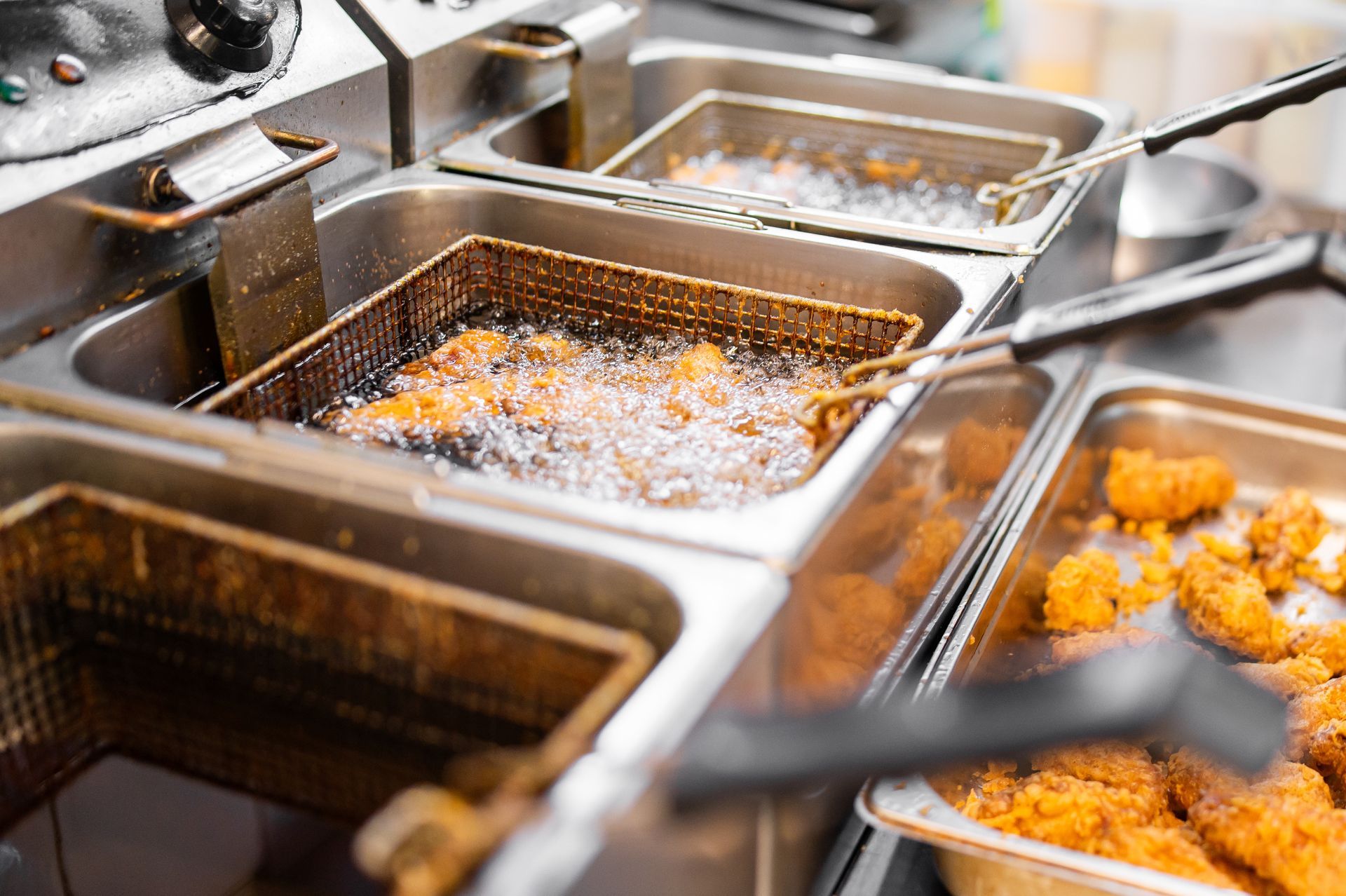 Frying station with several stainless steel pans of hot oil and breaded food cooking in a kitchen.