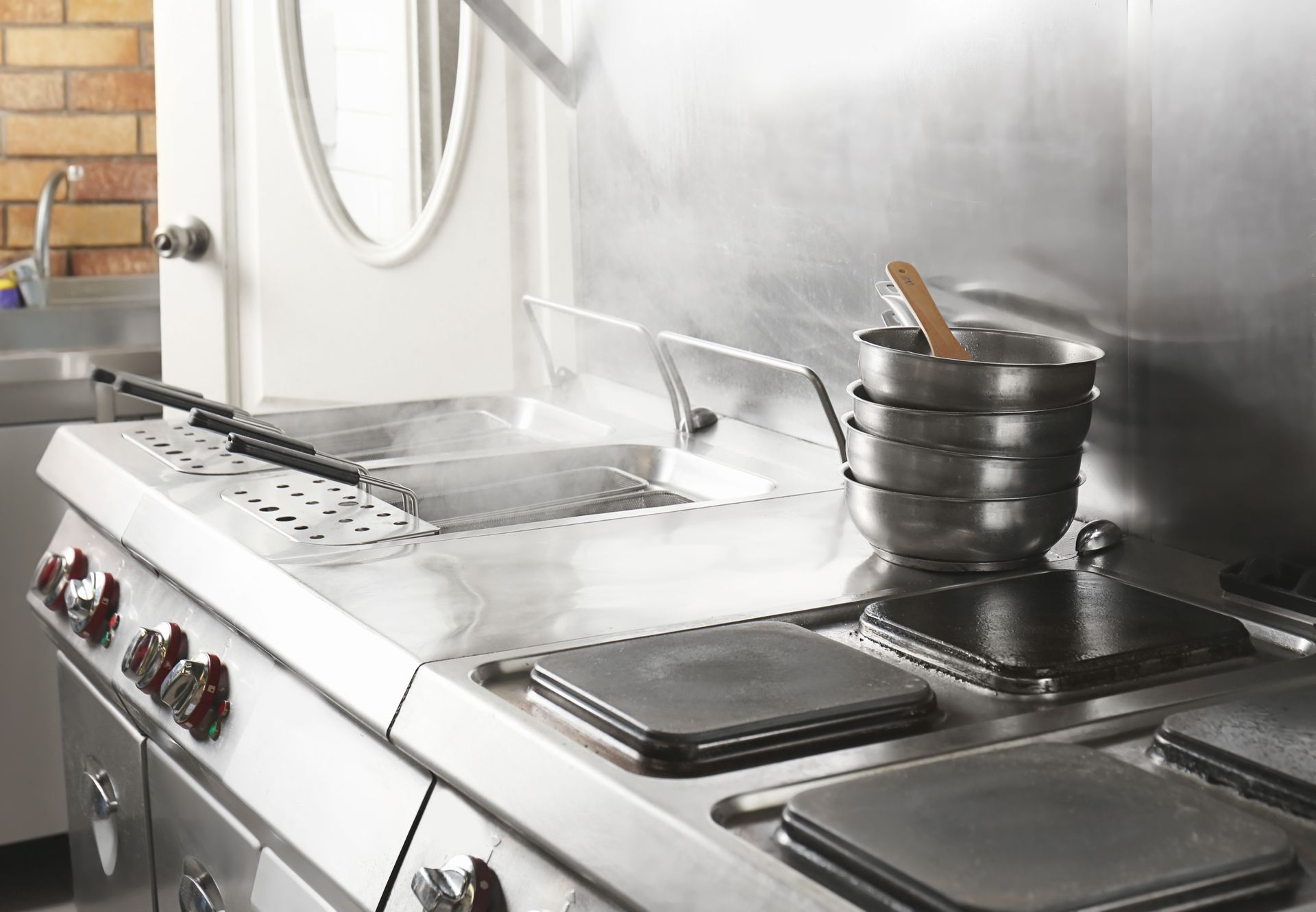 Stainless steel kitchen stove and range with pot, steam, and utensils on a counter.