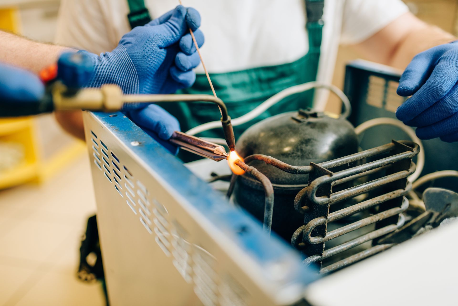 Gloved hands working on a metal cooking appliance with a pot and flames in a kitchen area.
