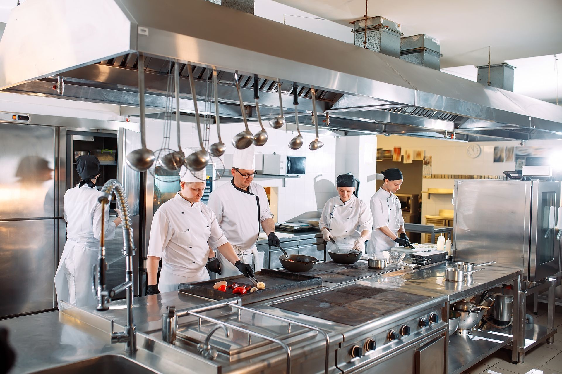 Commercial kitchen with stainless steel counters, racks, and equipment on a tiled floor.