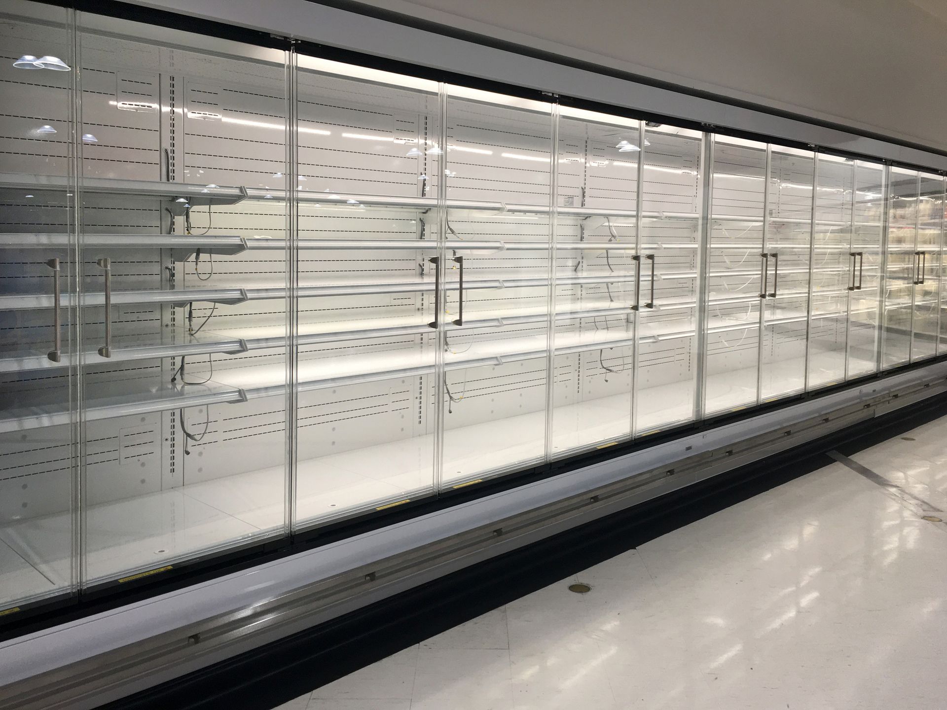 Empty refrigerated grocery aisle with glass doors and bright white shelves.