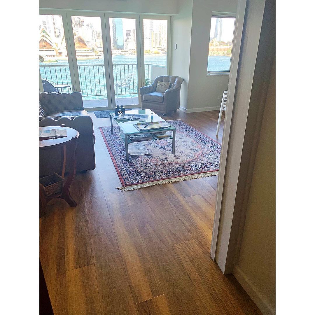 Bright living room with large windows, a patterned rug, coffee table, and blue armchairs on hardwood floors