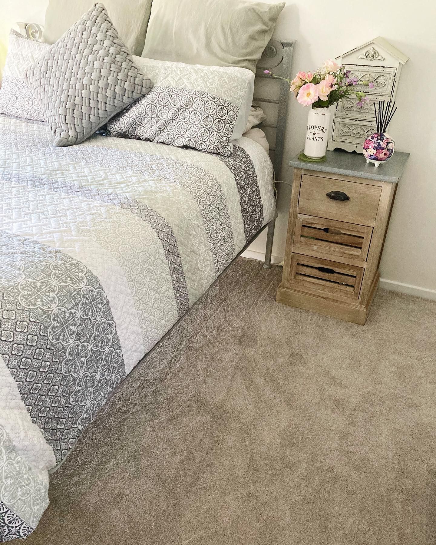 Cozy bedroom corner with a bed, patterned bedding, and a small bedside table with flowers